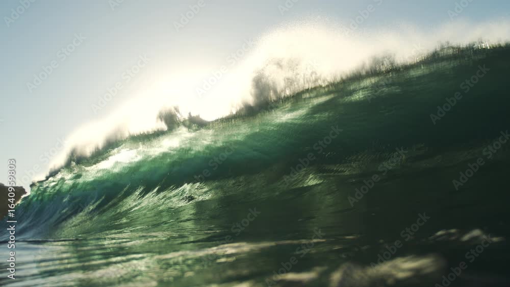 Poster wave curls and crashes with golden glow in slow motion