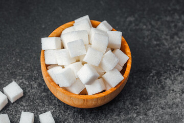 Cubes of sugar arranged in a wooden bowl on a dark surface