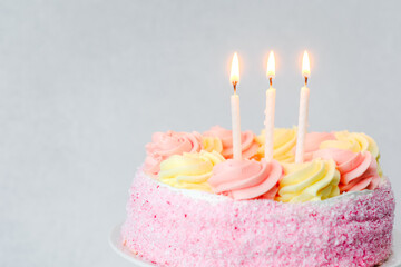 Birthday cake adorned with pink and yellow frosting and three candles lit