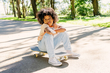 Playful child sitting on skateboard in park on a sunny day