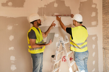 Two contractors using leveling tool and laptop working on construction site during a home renovation