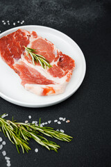 Uncooked beef steaks on white plate with rosemary and spices