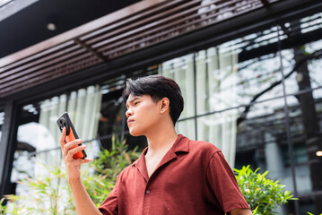 A focused young asian man intently using his phone to check directions on a maps app, carefully...