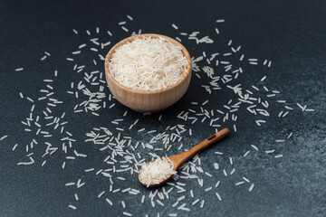 White rice in wooden bowl with scattered grains and wooden spoon
