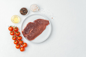 Raw beef steak on white plate with tomatoes and cooking ingredients