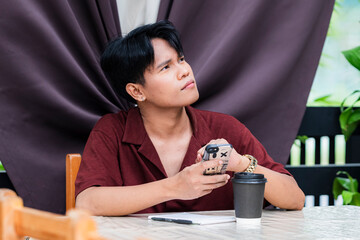 A contemplative young asian man gazing at the sky, immersed in imagination and deep thinking as he enjoys a serene moment at a cafe.