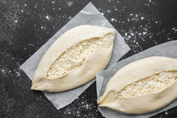 Closeup of two raw khachapuri with cheese on parchment paper and black background