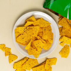 Crispy yellow corn tortilla chips served on a white plate, with some chips scattered around and a partially opened green package in the background.