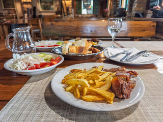 Traditional Balkan lunch with grilled meat, fried potatoes, fresh salad, and bread on a wooden...