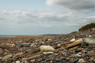 Coastal rocks embellish the tranquil shoreline under a cloudy sky near a distant lighthouse during...