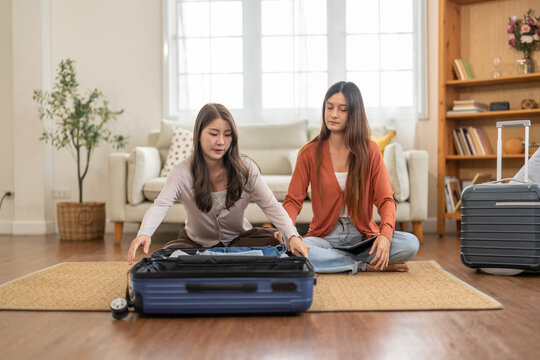 Young asian woman and friend preparing luggage packing clothes in suitcases for travel at home, planning holiday travel, content creator and travel blogger, friendship moments lifestyle vacation trip - Powered by Adobe
