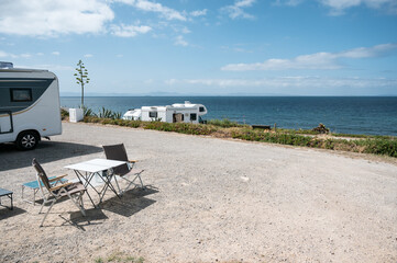 Campers enjoying ocean view from campsite with folding chairs and table