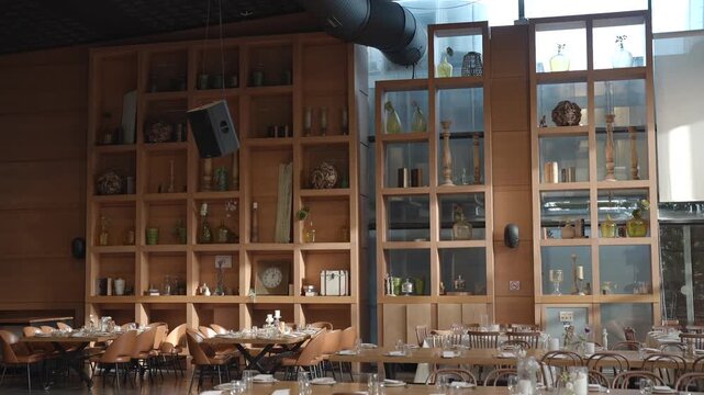 Modern restaurant interior featuring a large wooden shelving unit filled with decorative items and glassware. Tables are set gor guests' creating a warm and inviting atmosphere.