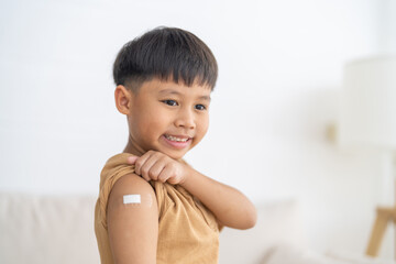 Portrait of happy smile vaccinated little asian kid boy children ages 5 to 11 years old posing show arm with medical plaster after Injection vaccine Covid-19 protection.coronavirus vaccination kid
