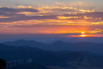 Wind turbines generating clean energy during a colorful sunset over mountains