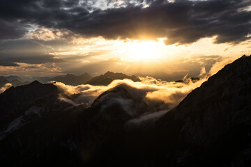 alpine mountain peaks under golden sunset sky. aerial view of mountain silhouettes in clouds by the golden sunset sky 