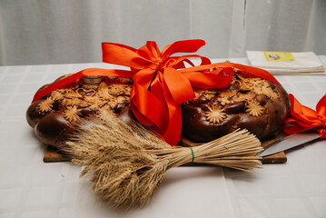 Two loaves of bread wrapped around each other with a red ribbon lie on an embroidered towel next to...