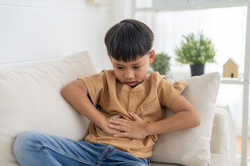 Portrait of sick unhappy little child asian boy touching belly stomach with suffering from stomach...