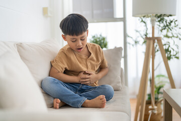 Portrait of sick unhappy little child asian boy touching belly stomach with suffering from stomach...