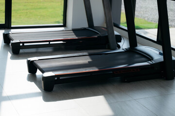 Two treadmills positioned near large windows in a modern gym, with natural sunlight casting shadows...