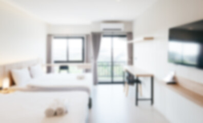 Out-of-focus image of a bright modern hotel bedroom with large beds, soft lighting, and sunlight...
