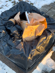 Black trash bag overflowing with recyclable and non-recyclable waste in a snowy outdoor location on...