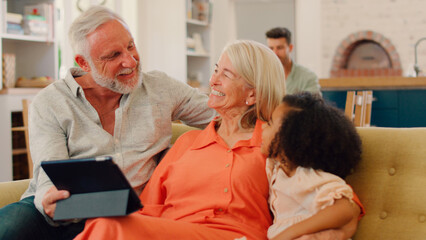 Fototapeta premium Granddaughter And Grandparents On Sofa At Home Streaming Show On Digital Tablet