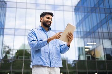 A smiling man is using a tablet outdoors, set against a modern office building.