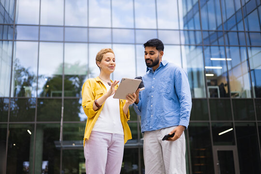 Two business professionals are reviewing a tablet outside a modern office building on a sunny day. - Powered by Adobe