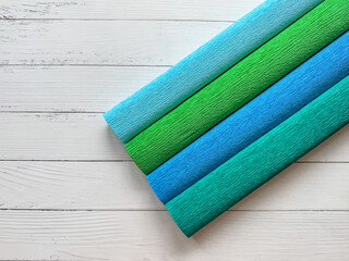 Four rolls of crepe paper in blue and green tones on light wooden background