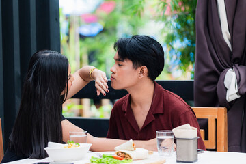 A sweet young Asian woman gently trying to wipe the mouth of her loving young Asian man as they share a tender moment, clearly in love and enjoying their affectionate connection together at a cafe