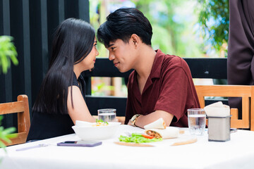 An affectionate young Asian man and young Asian woman with their foreheads almost touching, looking sweetly into each other, clearly in love and sharing a tender, intimate moment together at a cafe