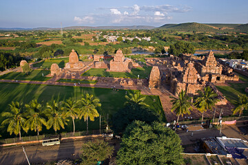 Aerial view of ancient temples bathed in the warm glow of sunset, casting long shadows across manicured lawns, Pattadakal, Karnataka, India.