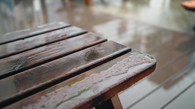 Wet wooden table with rain drops splashing and creating ripples on the surface outdoors
