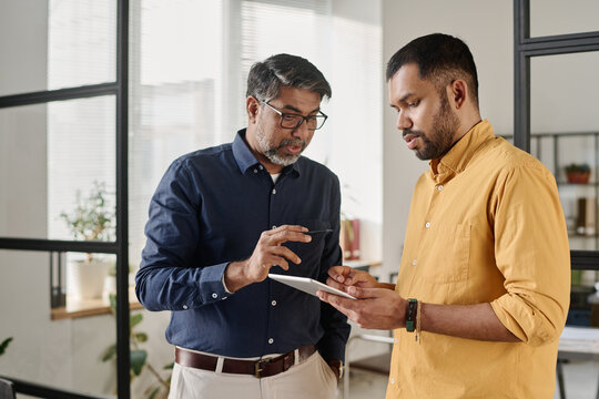 Medium shot of two Indian men standing in office looking at digital tablet screen discussing business plan - Powered by Adobe