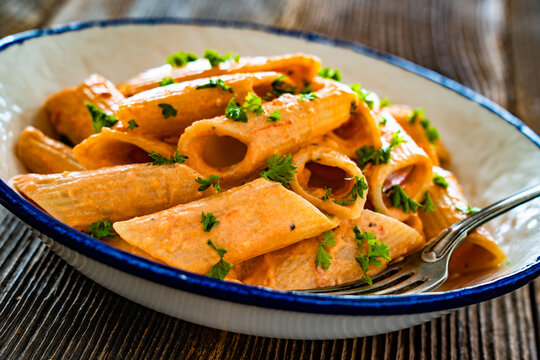 Creamy tomato and stracciatella pennone rigato noodles on wooden table