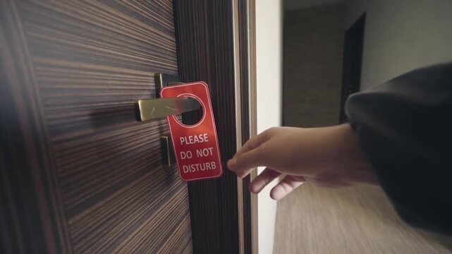 Customer hand places a red 'Do Not Disturb' sign on a hotel door handle, signaling privacy