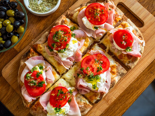 Pinsa Romana with boiled ham, burrata cheese, tomatoes on wooden table