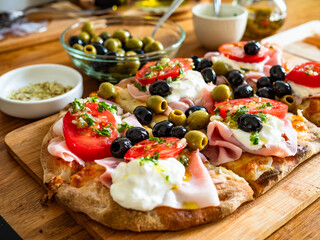 Pinsa Romana with boiled ham, burrata cheese, tomatoes and olives on wooden table