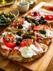 Pinsa Romana with boiled ham, burrata cheese, tomatoes and olives on wooden table