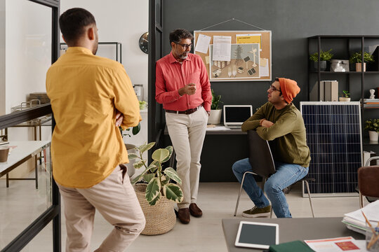 Group of three South Asian developers standing and sitting in modern office discussing new project