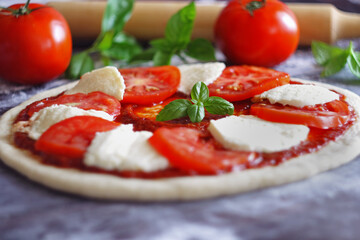 Raw Caprese pizza with tomato, mozzarella and basil leaves. Selective focus
