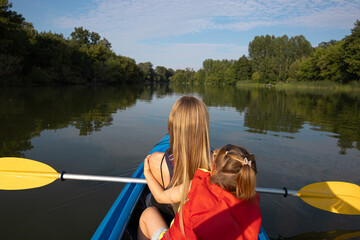 Mother and daughter paddling a canoe on calm river in summer nature