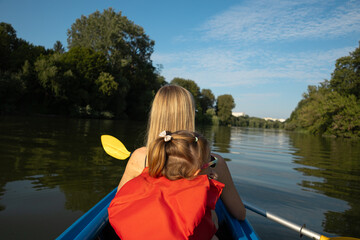 Mother and daughter paddling a canoe on calm river in summer nature