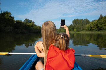 Mother and daughter canoeing on a river and taking a selfie on their phone