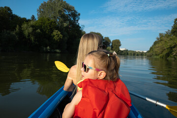 Mother and daughter paddling a canoe on calm river in summer nature