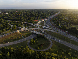 Aerial view of the intricate highway interchange weaving through a tapestry of lush green trees under the soft glow of the setting sun, Charlotte, North Carolina, United States.