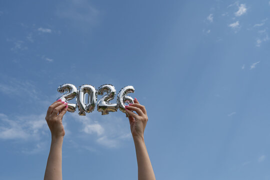Hands holding silver 2026 balloons against clear sky