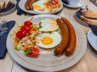 Breakfast for two served in a restaurant, with a focus on a plate of fried eggs, savory sausages,...