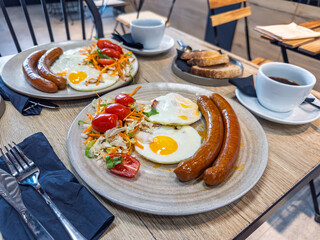 A delicious breakfast for two served at a modern cafe, featuring fried eggs, sausages, fresh salad,...